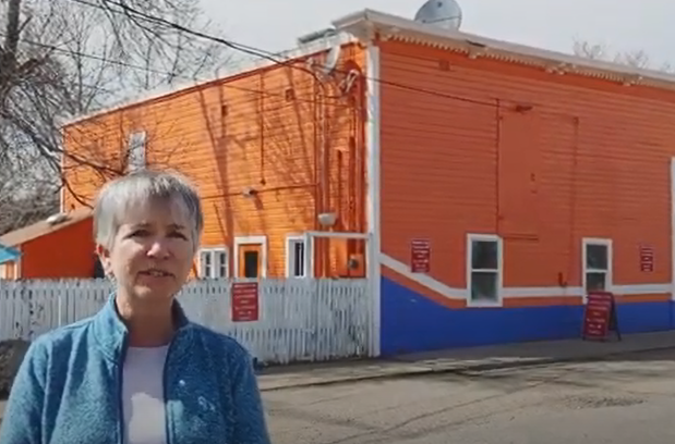 A woman stands in front of a bright orange and blue building that houses Casa Alegre Restaurant