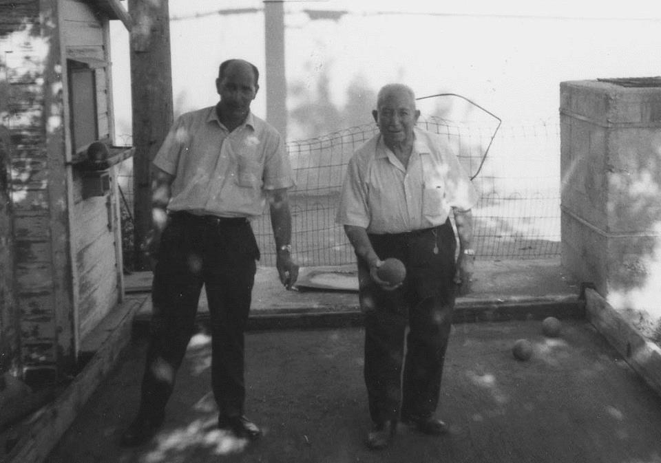 black and white image of two older men standing on a bocce court. One is holding a bocce ball.