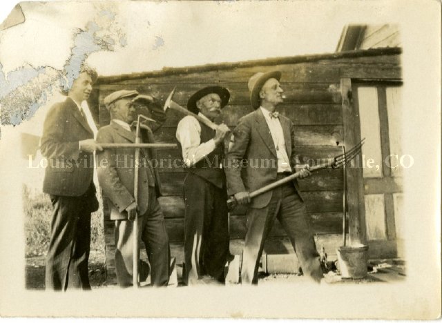 Four men in suits carrying garden tools.