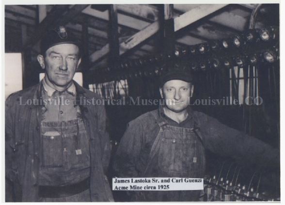 Two men in overalls standing in front of a line of helmet lights from the Acme Mine