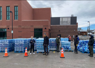 Recovery workers distributing bottled water in front of a brick building