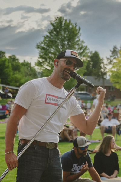 Man singing into microphone in front of crowd in park