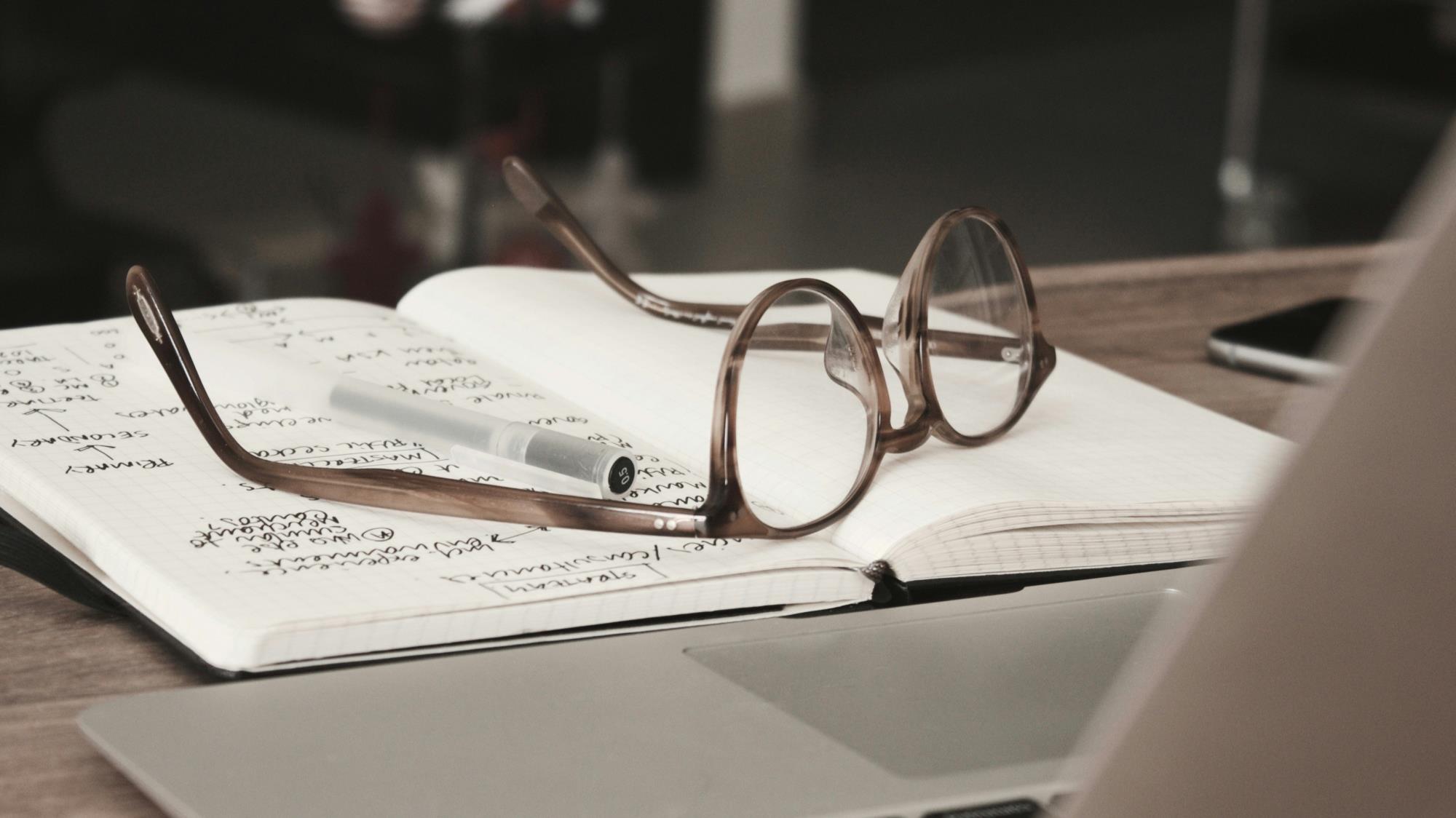Notebook lying open on table with glasses on top.