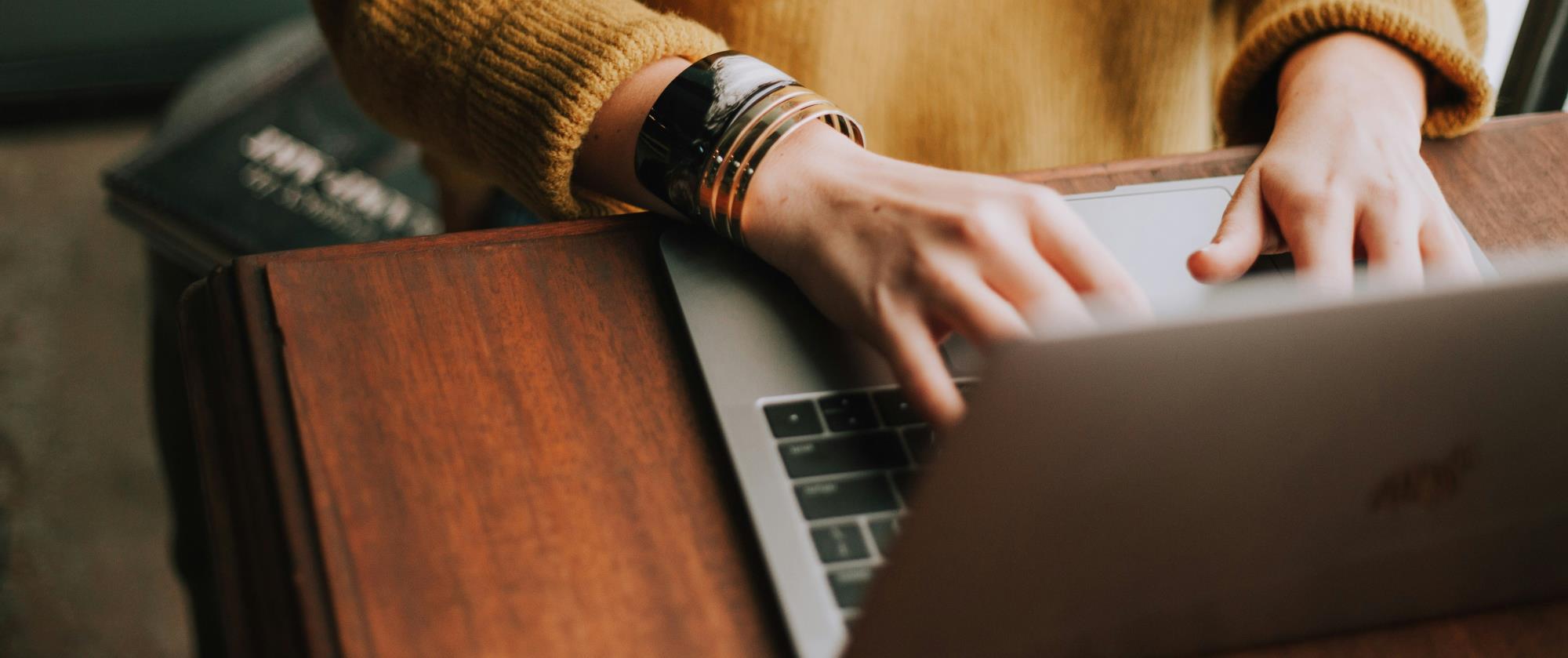 Person in yellow sweater typing on laptop.